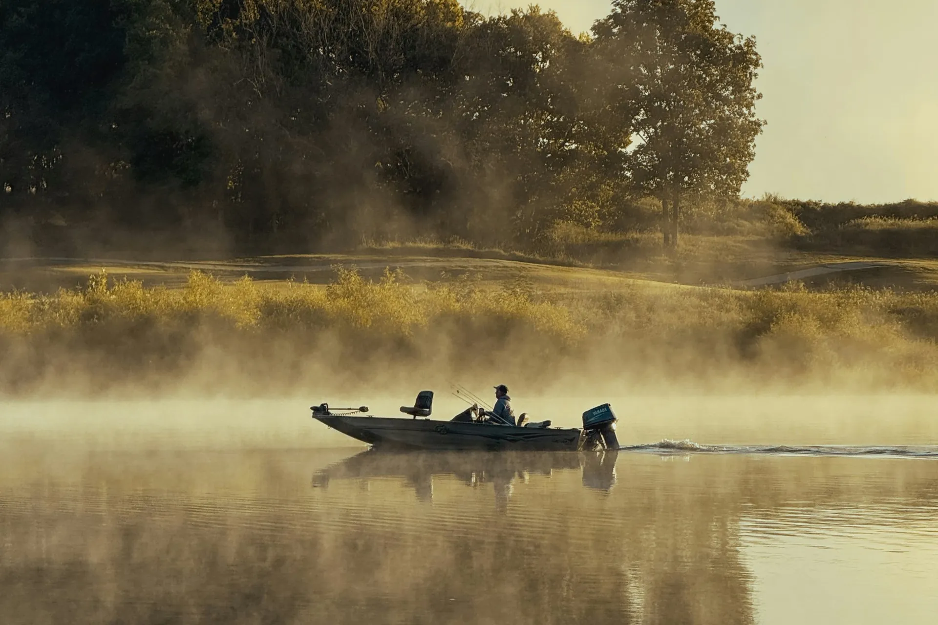 fishing boat crossing a misty lake at sunrise