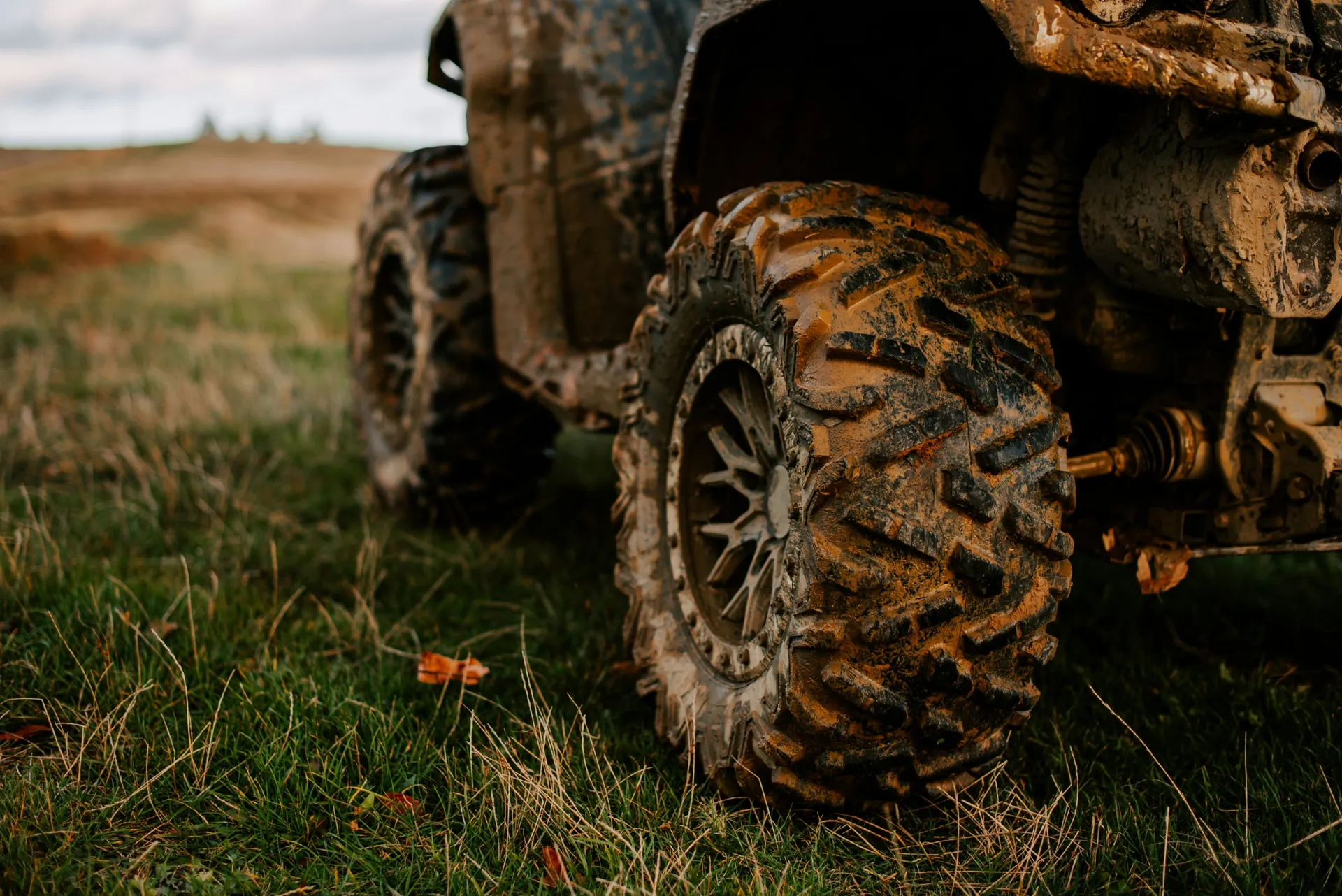 Close-up of a mud-covered ATV tire parked in a grassy field