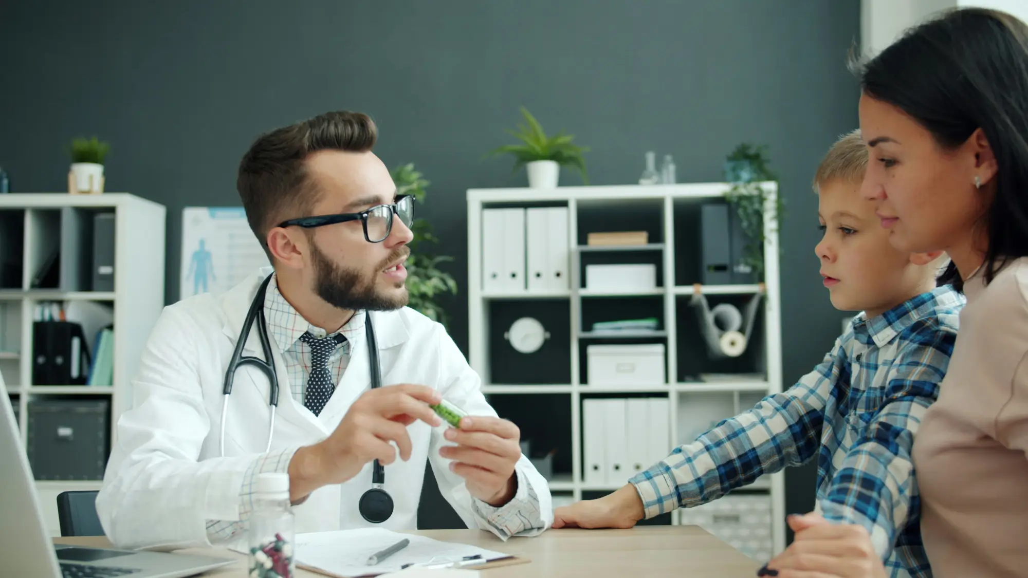 A doctor holds a medication bottle while talking with a mother and child in an exam room