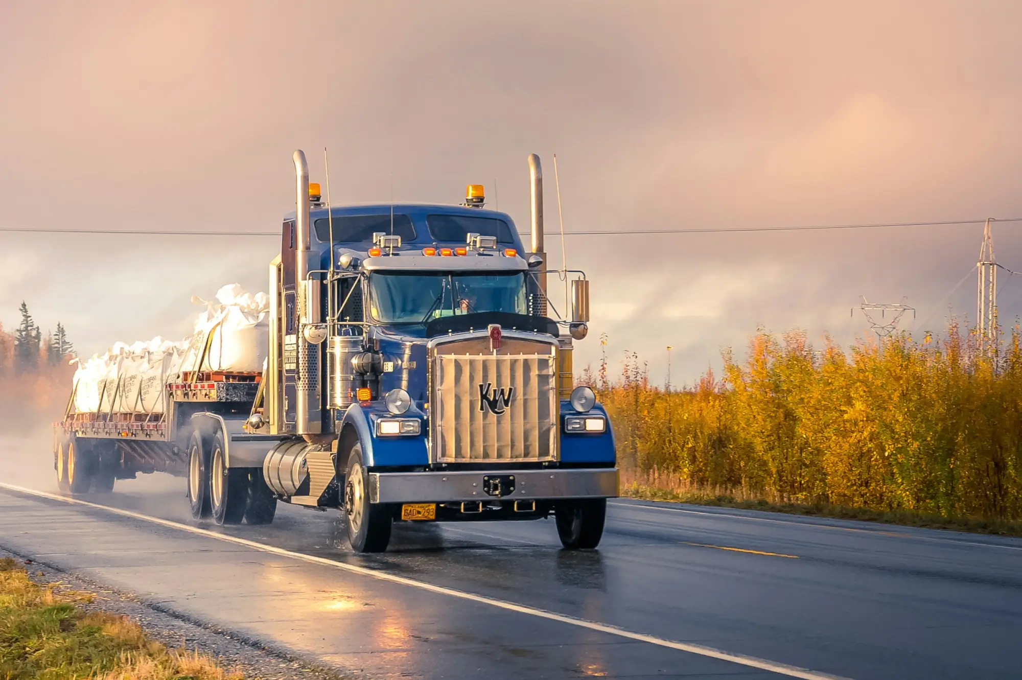 18-wheeler truck on the road with clouds and bright foliage in the background.